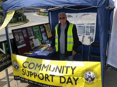A person standing behind a stall with the banner community support day